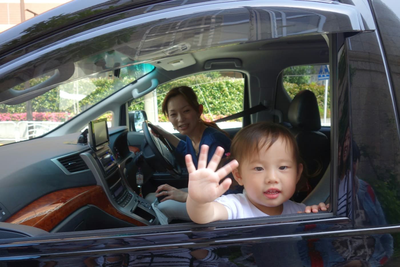 Criança acenando pela janela do carro com a mãe ao volante