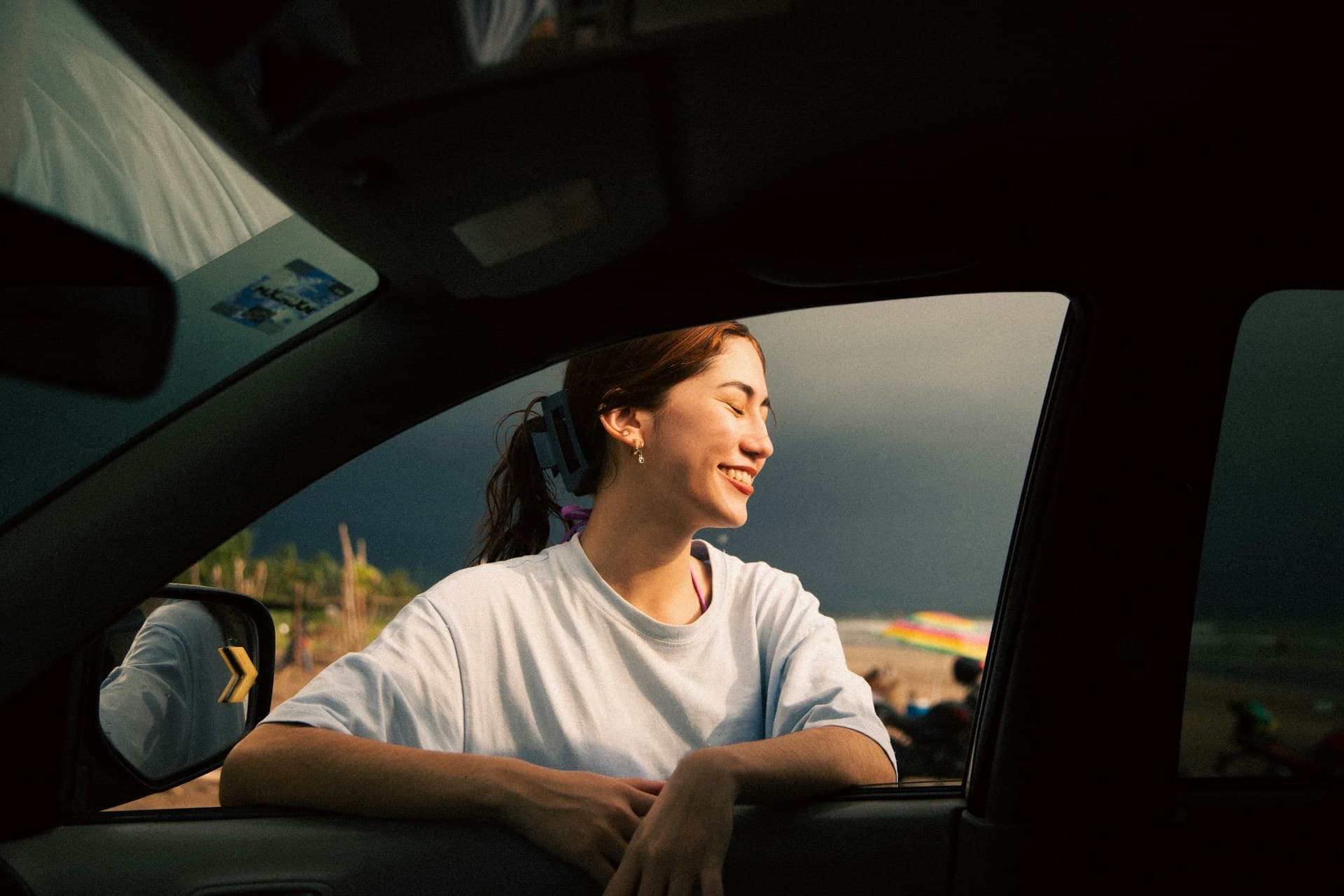 Jovem sorrindo apoiada na janela do carro ao pôr do sol