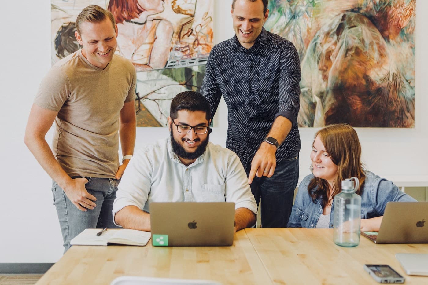 Quatro colegas de trabalho sorrindo em volta de um notebook