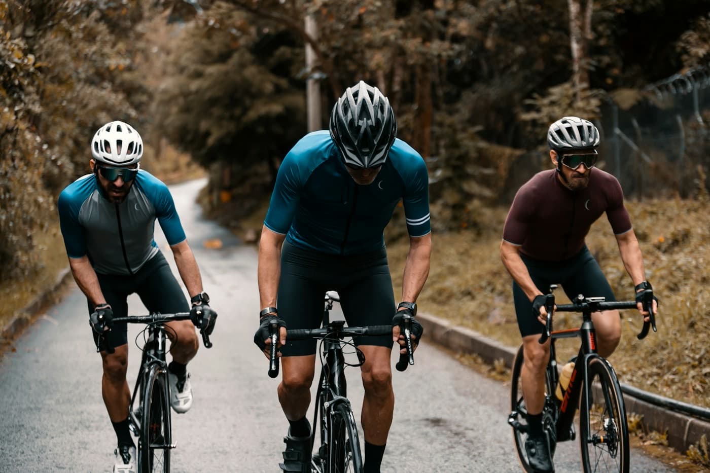 Três ciclistas de capacete pedalando lado a lado em uma estrada