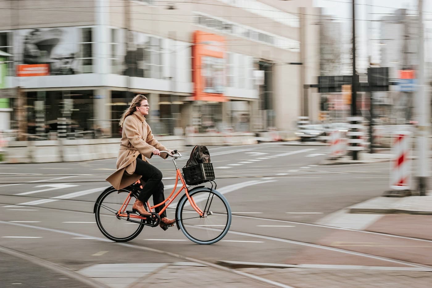 Mulher de casaco pedalando uma bicicleta urbana pelo centro da cidade