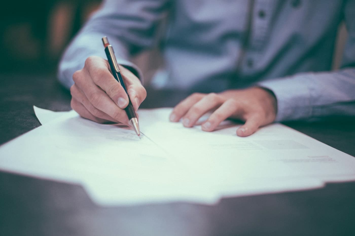 Mão assinando um documento com uma caneta