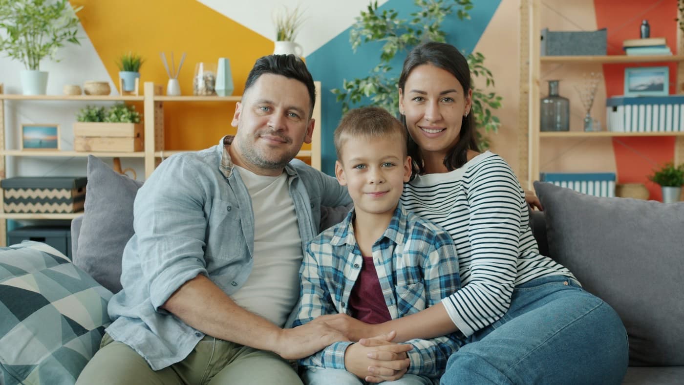 Família sorrindo abraçada no sofá de casa
