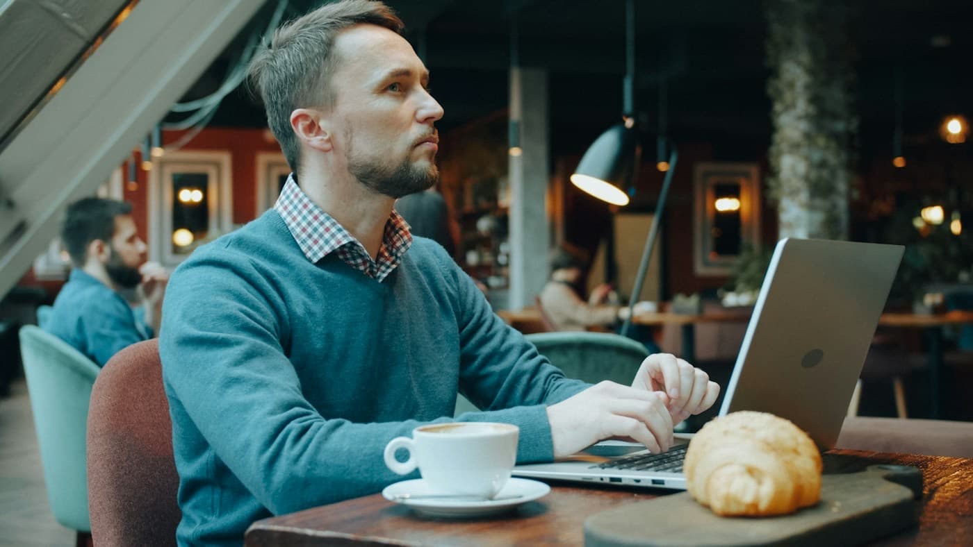 Homem trabalhando no notebook em uma cafeteria, com uma xícara de café ao lado