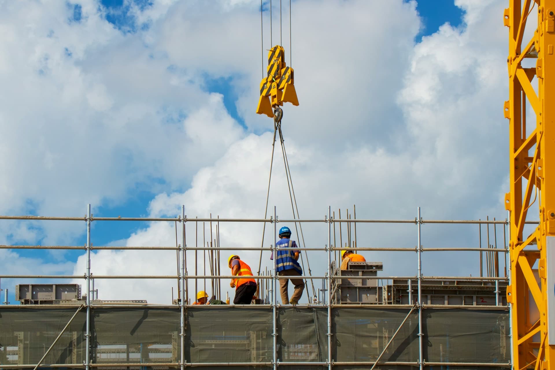 Equipe de operários trabalhando no alto de uma obra, com grua ao fundo