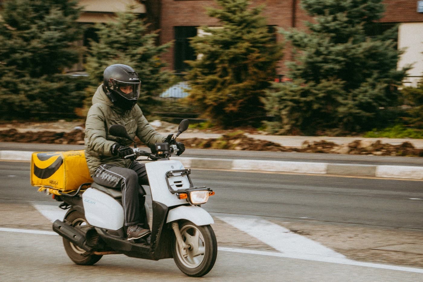 Entregador pilotando uma moto com baú em uma rua