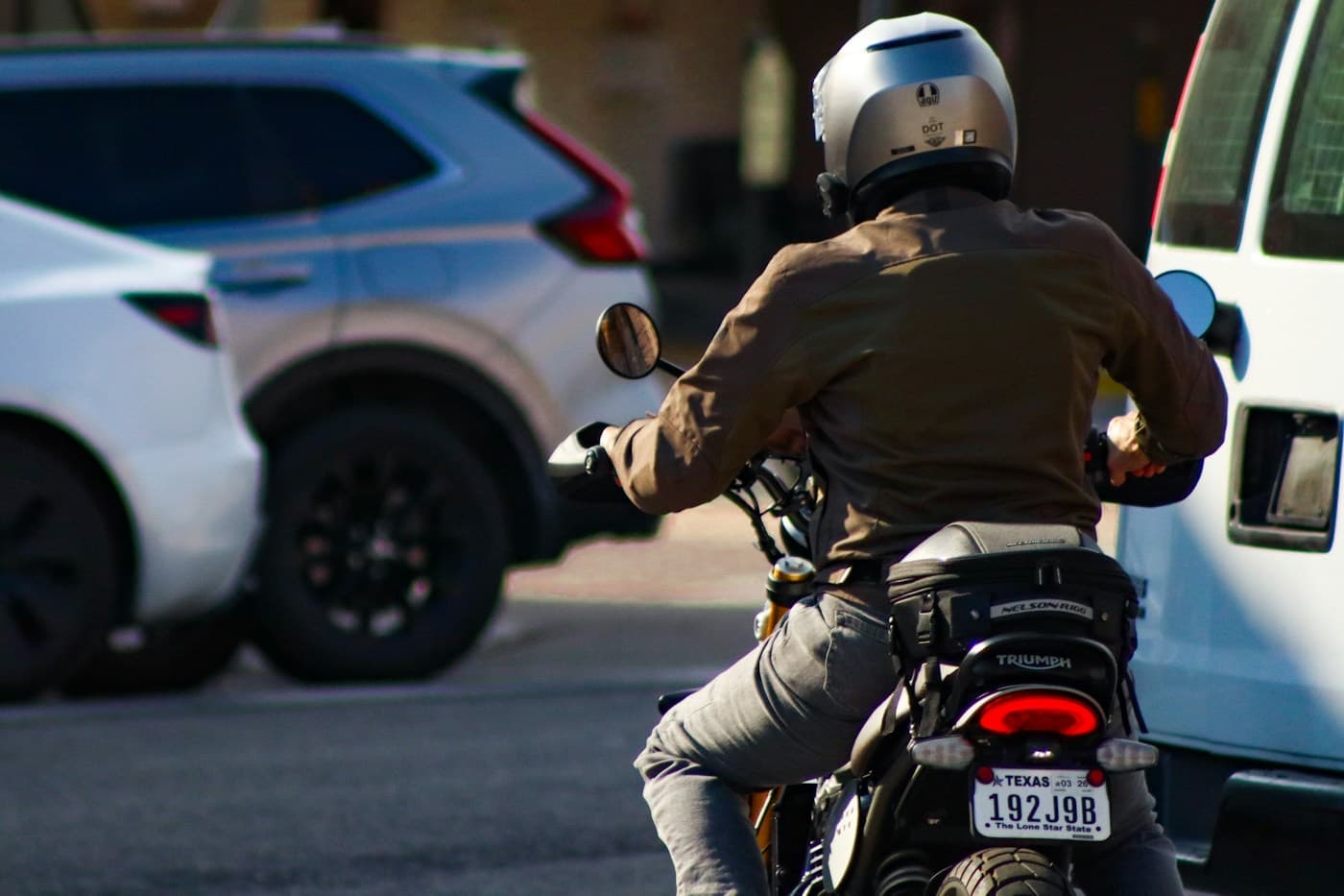 Motociclista de capacete passando entre os carros no trânsito