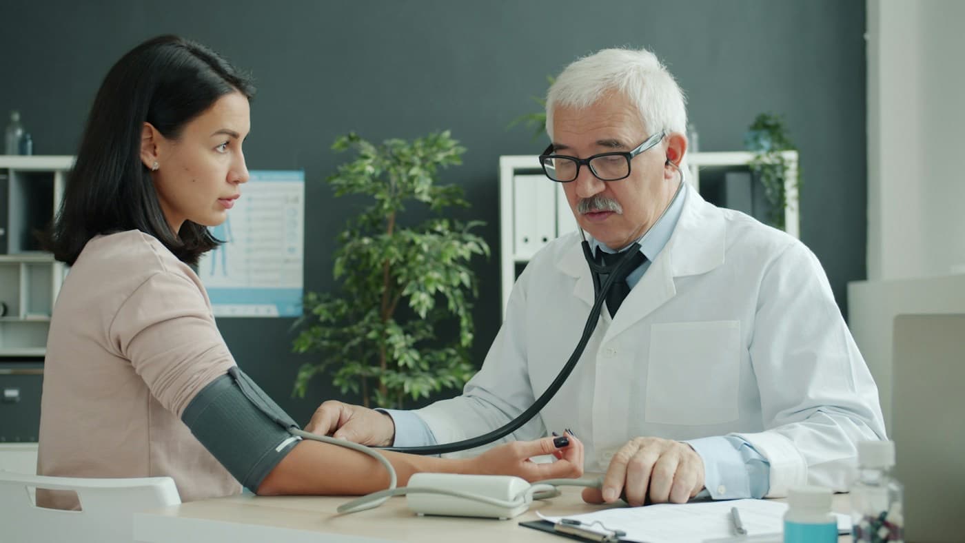 Médico aferindo a pressão de uma paciente no consultório