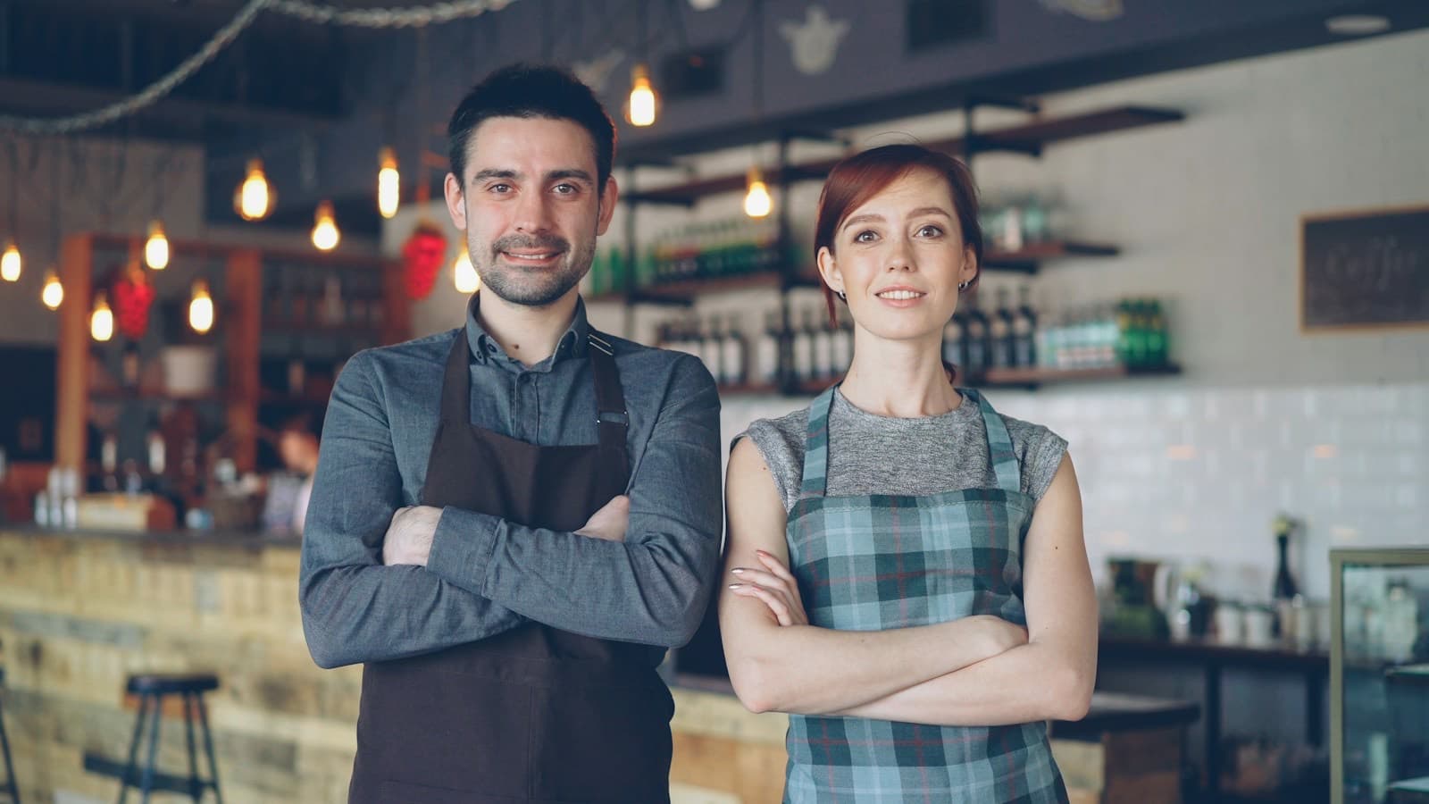 Casal de empreendedores de avental em frente ao balcão do seu café