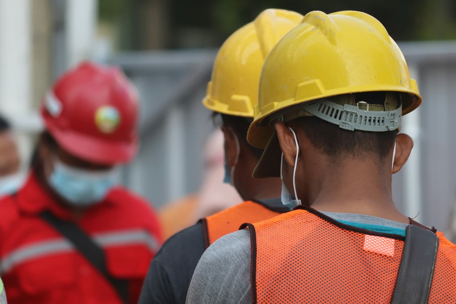 Trabalhadores com capacete e colete de segurança em área industrial