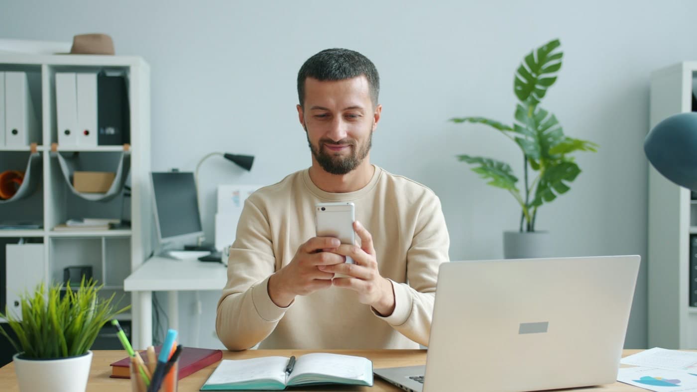 Colaborador sorrindo enquanto responde a uma pesquisa pelo celular na sua mesa