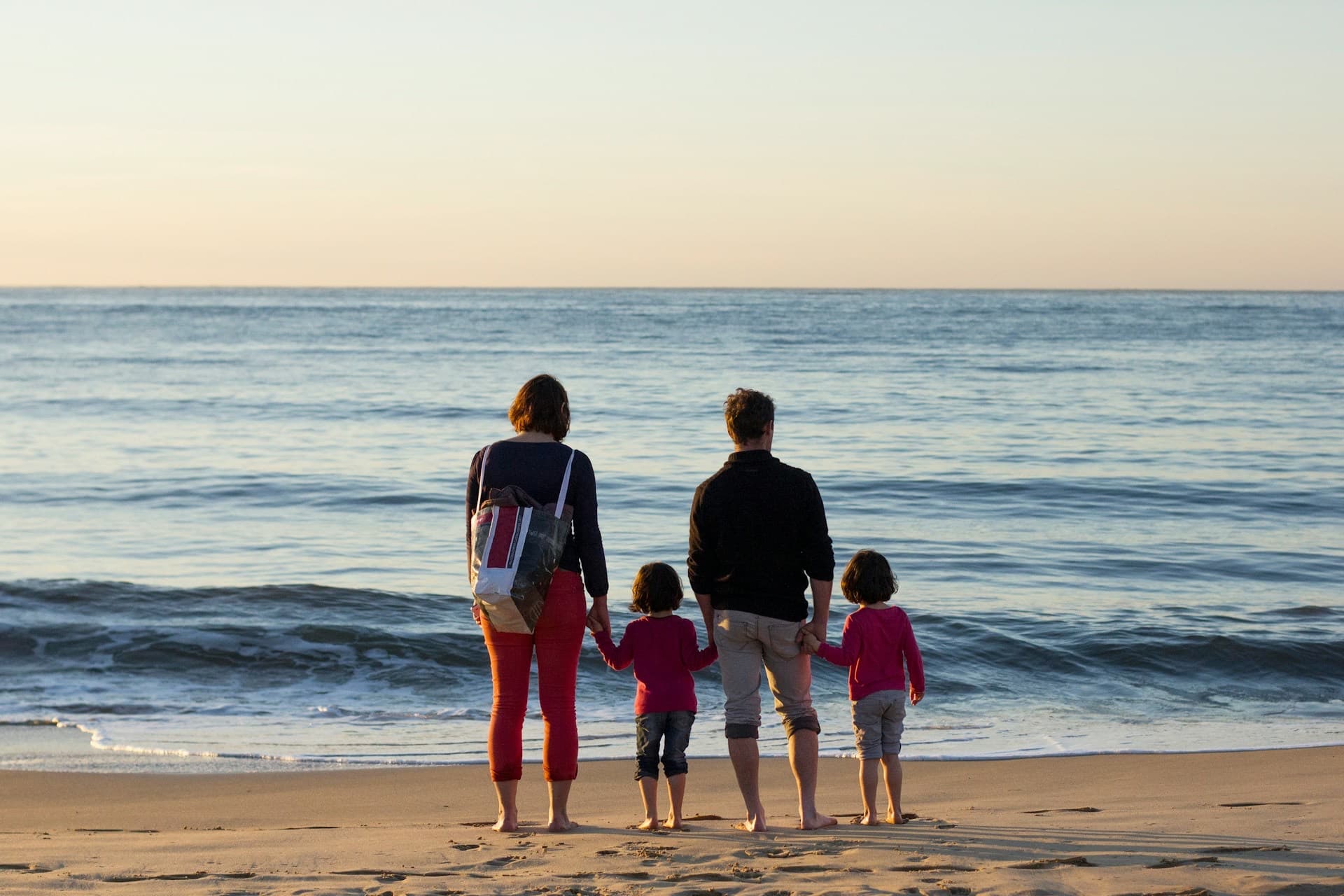 Família de mãos dadas à beira do mar, de costas, olhando o horizonte